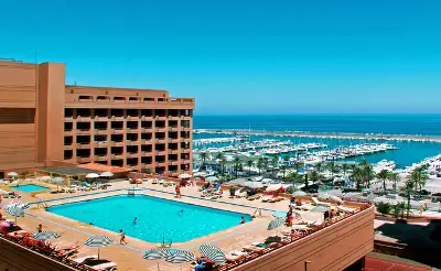 Hotel Las Palmeras in Fuengirola featuring a large rooftop pool, sun loungers, and views of the marina and Mediterranean Sea.