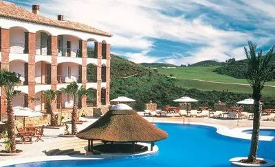 La Cala Hotel with a large outdoor pool, sun loungers, and thatched poolside bar set against a backdrop of rolling green hills.