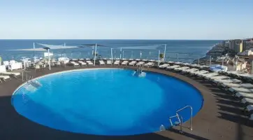 Circular rooftop pool with sun loungers at Hotel El Puerto offering panoramic views of the sea.