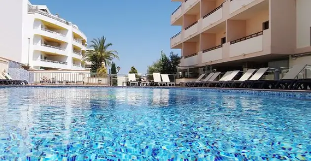 Invisa Hotel La Cala in Ibiza featuring a clear blue swimming pool surrounded by sun loungers and balconies under a sunny sky.