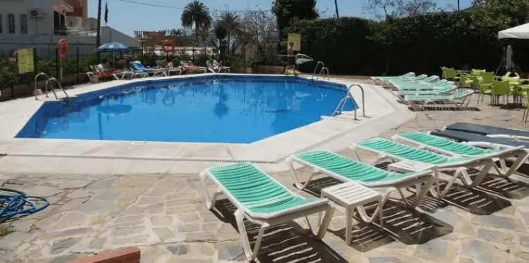 Outdoor swimming pool with sun loungers at Doramar Apartments, surrounded by greenery and located in a peaceful setting.