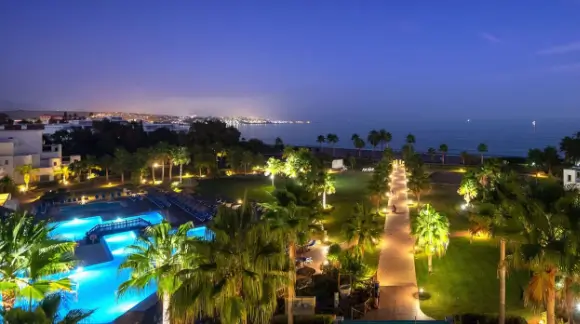 Night view of Estepona Hotel and Spa with illuminated pathways, palm trees, and a glowing outdoor pool overlooking the sea.