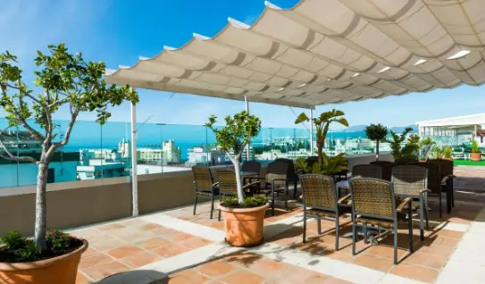 Rooftop terrace at Hotel El Rodeo with shaded seating area, potted plants, and views of the city and harbour.